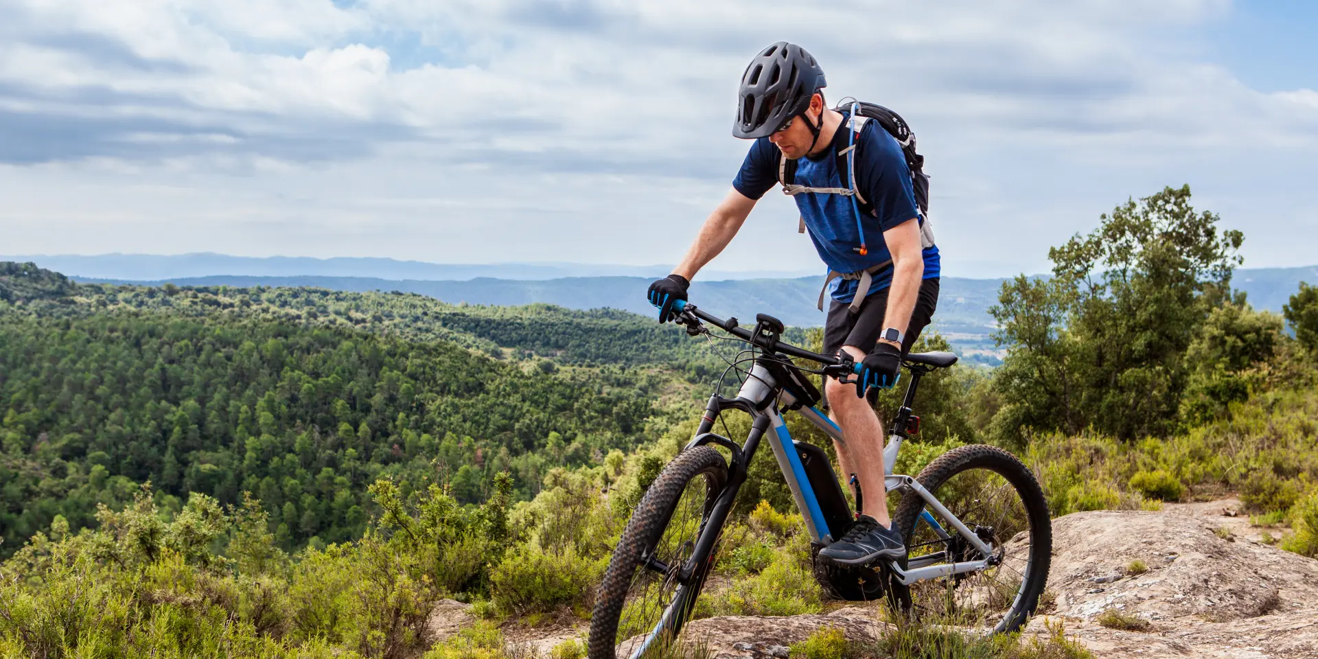 Male mountain biker balancing his ebike on a rock, nice landscape in the background