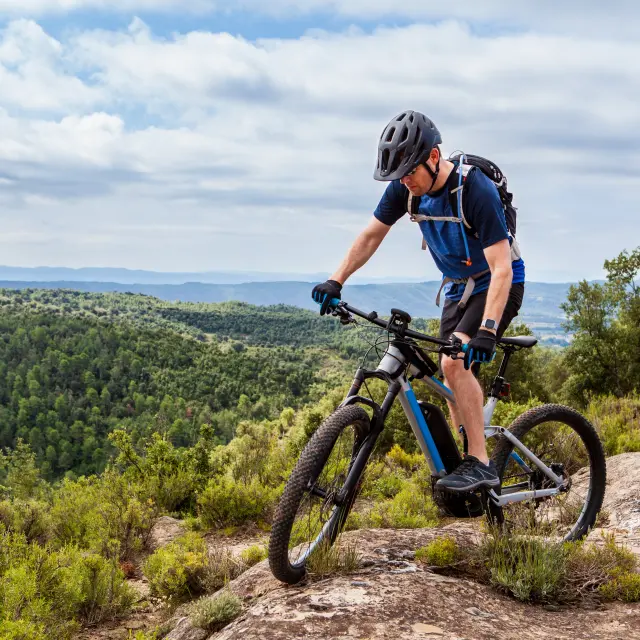 Male mountain biker balancing his ebike on a rock, nice landscape in the background