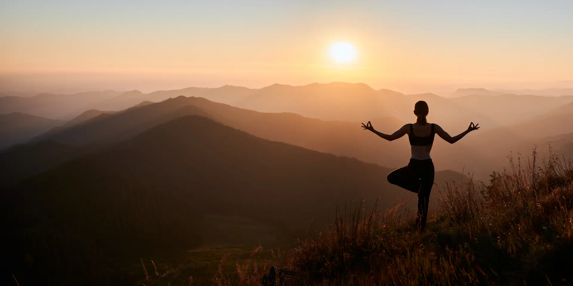 Panoramic view. Back view of slim woman in black sportswear doing yoga exercise on one leg in mountains. Concept of yoga time at sunset.