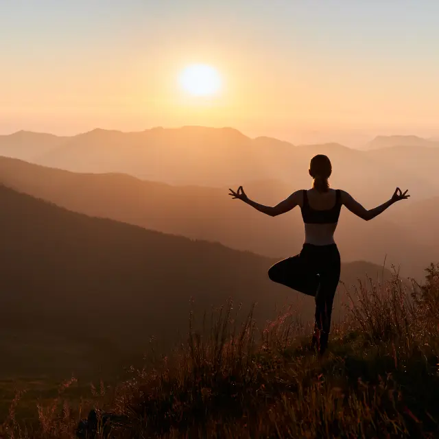 Panoramic view. Back view of slim woman in black sportswear doing yoga exercise on one leg in mountains. Concept of yoga time at sunset.
