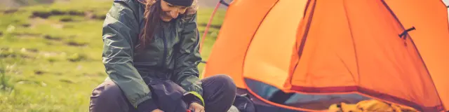 alpine woman folding sleeping bag and other accessories for camping. In the background orange tent and equipment for outdoor activities.